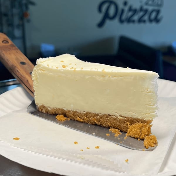 A slice of New York cheesecake with a graham cracker crust on a metal server.