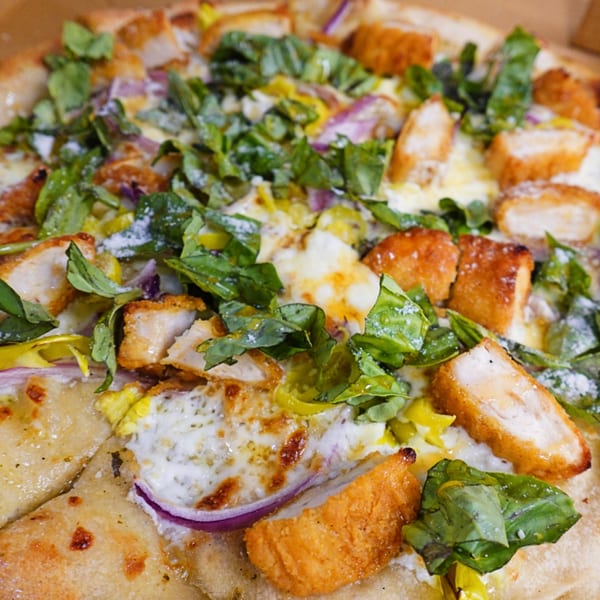 Close-up of a Saruzzo's New York Pizzeria pizza topped with crispy chicken, red onion, and fresh greens.