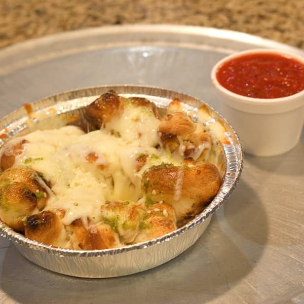 Cheesy garlic knots in a foil pan with a side of marinara sauce on a metal tray.