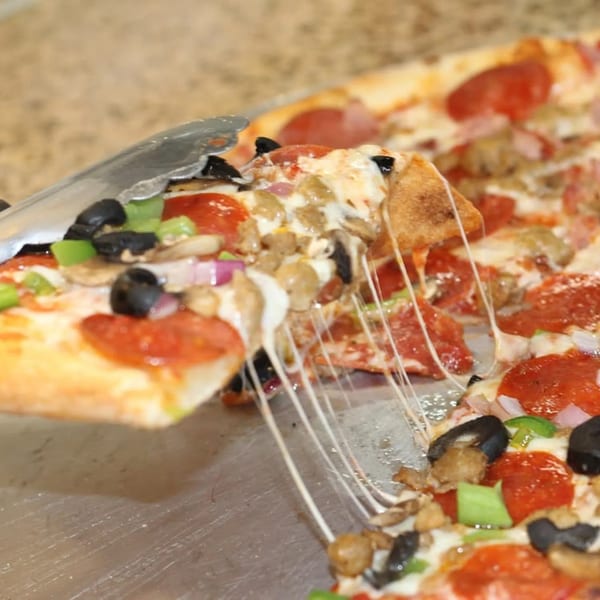 A slice of Saruzzo's New York Pizzeria's supreme pizza is lifted, stretching cheese.