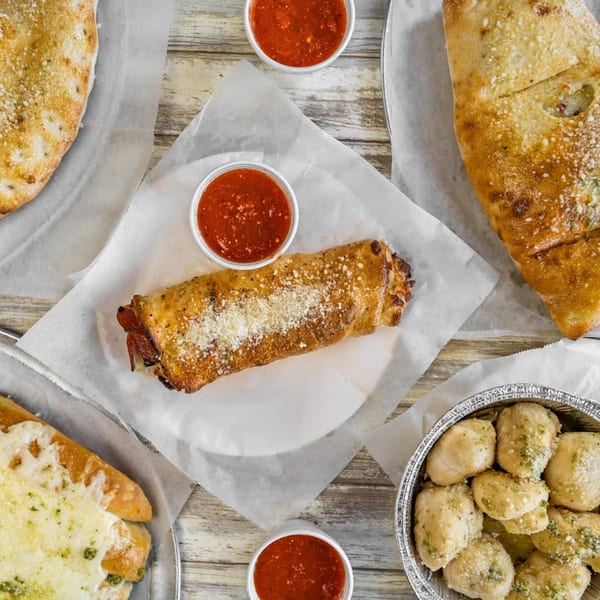 An overhead view of Saruzzo's New York Pizzeria calzones, stromboli, garlic knots, and marinara sauce.