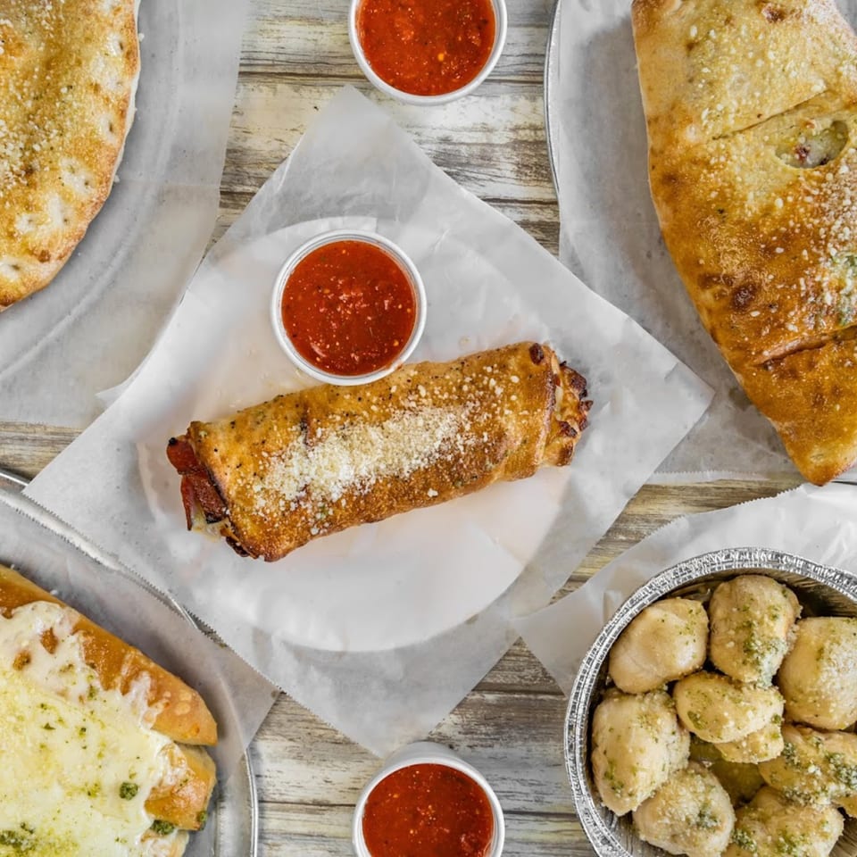 An overhead view of Saruzzo's New York Pizzeria calzones, stromboli, garlic knots, and marinara sauce.