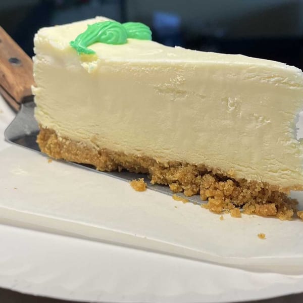 A slice of Saruzzo's New York cheesecake with a graham cracker crust and green frosting.