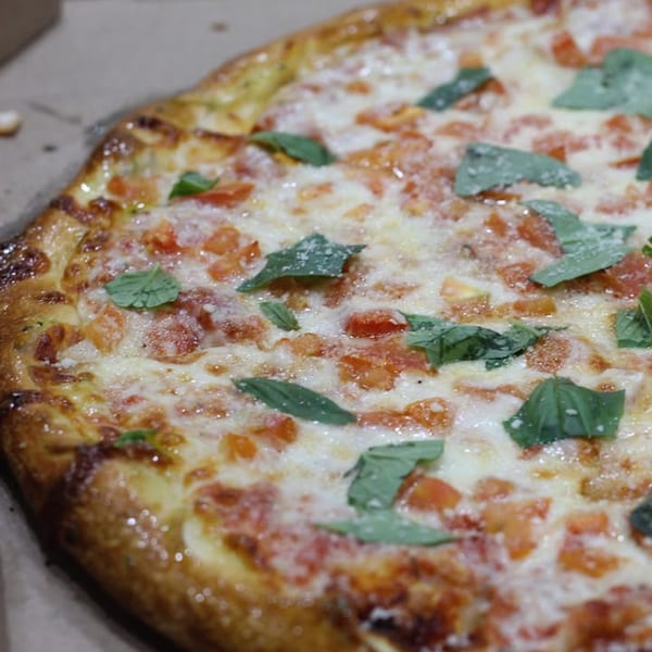 Close-up of a Saruzzo's New York Pizzeria Margherita pizza with fresh basil and diced tomatoes.